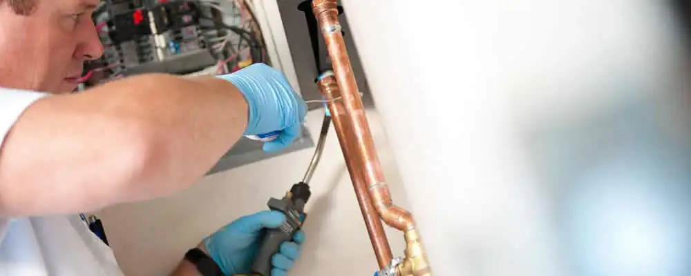 Water heater repair technician testing copper pipe connections and controls in Hoboken, NJ